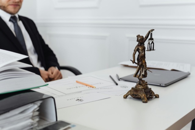 Notary public at a desk with certificates and a Lady Justice statue.