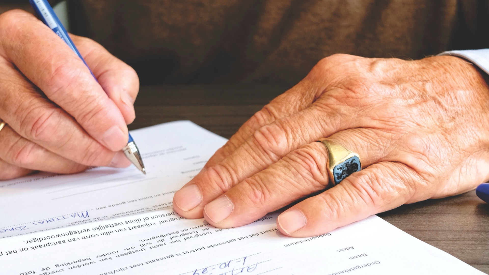 An older man's hands signing a legal document at a desk.
